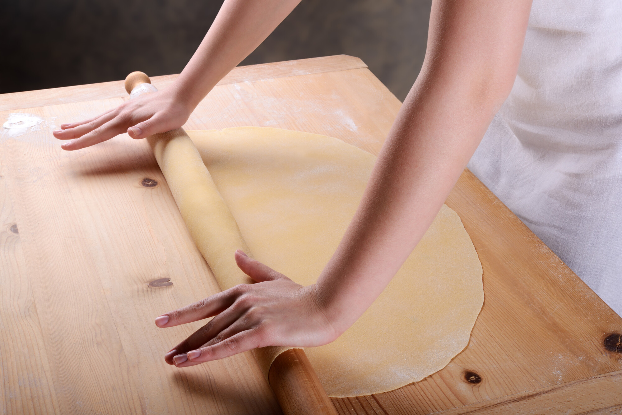 Mani stendono col mattarello una sfoglia gialla sottile sulla spianatoia di legno infarinata da Pasta Fresca Farini